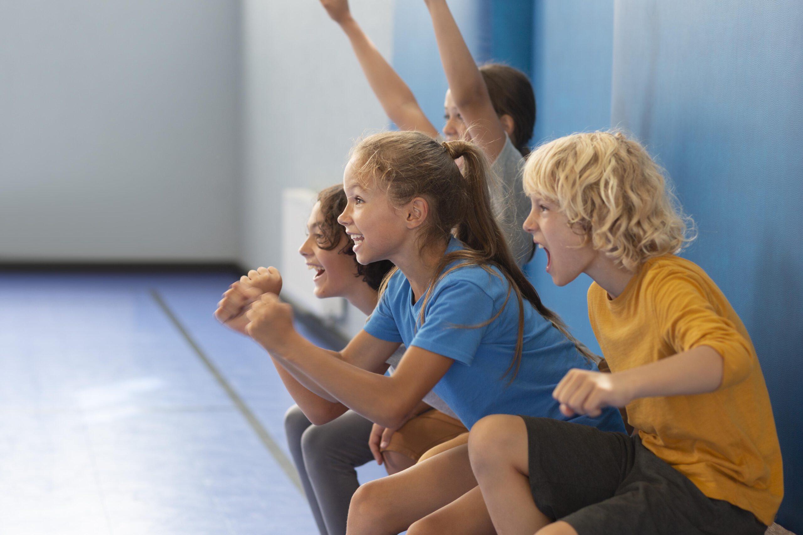 Vorschul-/Kinderturnen Lachende Kinder in Sportkleidung sitzen auf einer Bank in der Turnhalle