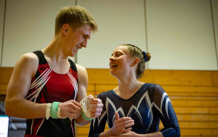 Turner und Turnerin des TV Wolfenweiler-Schallstadt in Wettkampfanzügen lachen sich in der Turnhalle an